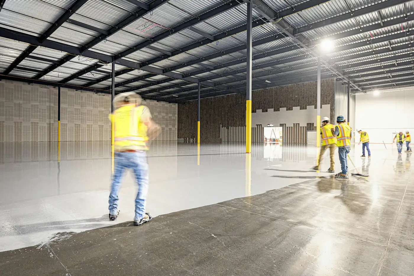 Crew applying a gray epoxy coating across a large warehouse floor